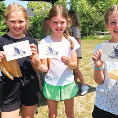 Three girls proudly display their windmill prints made at a hands-on craft station during NHA Community Day, a free family event on Nantucket.