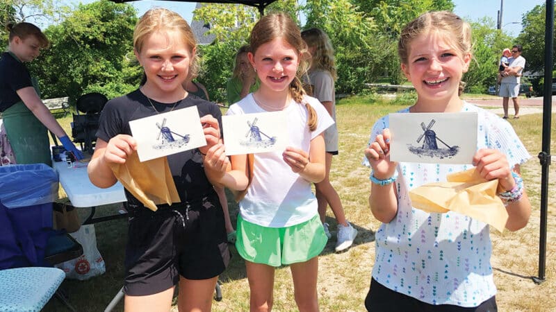 Three girls proudly display their windmill prints made at a hands-on craft station during NHA Community Day, a free family event on Nantucket.