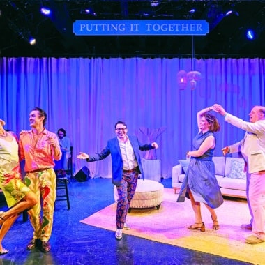 The cast of Putting It Together dances and performs on stage at the Theatre Workshop of Nantucket, with the show's title sign lit above a coastal mansion set.
