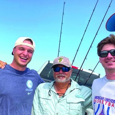 Nantucket fishing guide Steve Tuna Tornovish poses with three clients on a sunny beach with surf fishing rods loaded on a truck behind them.