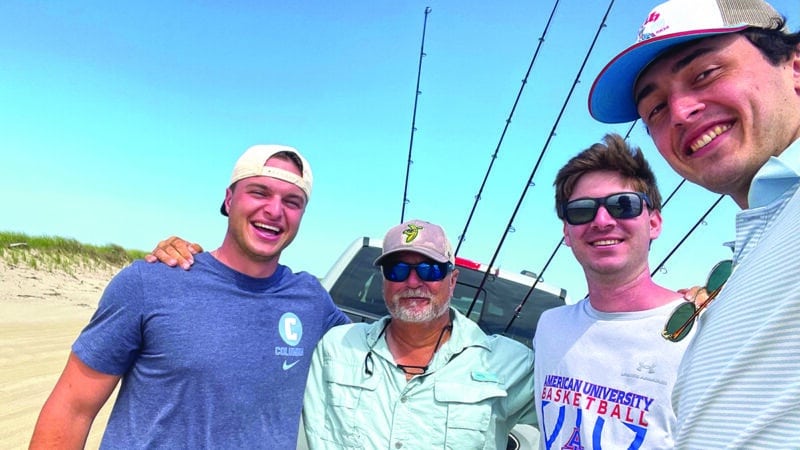 Nantucket fishing guide Steve Tuna Tornovish poses with three clients on a sunny beach with surf fishing rods loaded on a truck behind them.