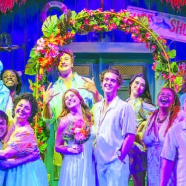 The cast of Theatre Workshop of Nantucket's Escape to Margaritaville poses on the show's vibrant tropical set.