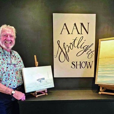 Nantucket artist G.S. Hill stands beside two of his oil paintings on display for the AAN Spotlight Series show.