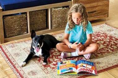 A young girl reads a picture book with her dog beside her, reflecting the love of reading Nantucket Children's Book Day hopes to inspire.