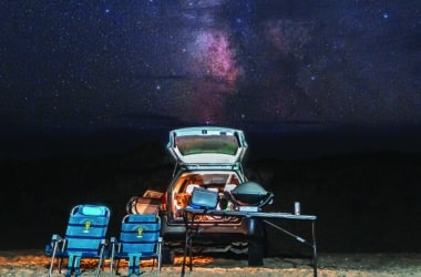 The Milky Way blazes over a Nantucket beach camp setup, the kind of dark sky the essay describes discovering at night.