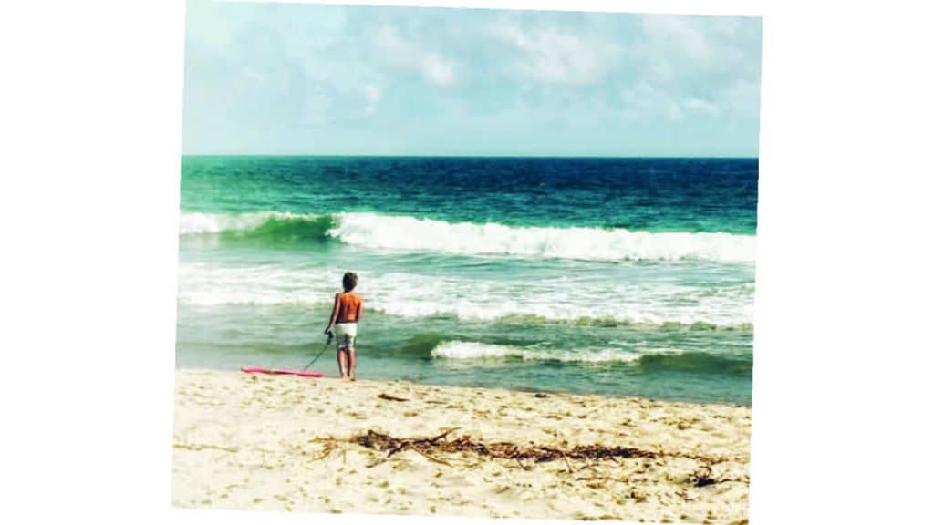 A boy pauses at the water's edge with his bodyboard, capturing the quiet brilliance of summer on Nantucket.