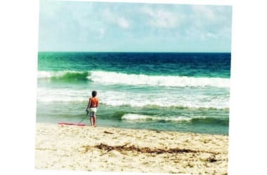 A boy pauses at the water's edge with his bodyboard, capturing the quiet brilliance of summer on Nantucket.