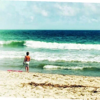 A boy pauses at the water's edge with his bodyboard, capturing the quiet brilliance of summer on Nantucket.